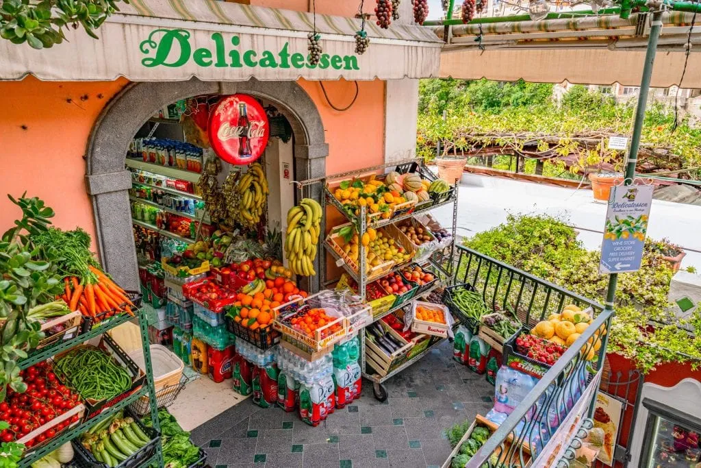 Fruit stand in Positano as shot from above. An overhang says "Delicatesen" in green letters and a coca-cola sign hangs below that.