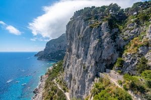 Cliffs of Capri with bright blue water and boats visible to the left. Definitely consider a visit here when planning a trip to Italy!