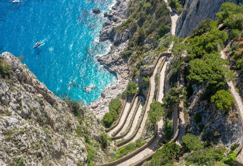 Photo of a winding road on Capri shot from above. You can see cliffs in the bottom of the photo and bright blue sea in the upper left.