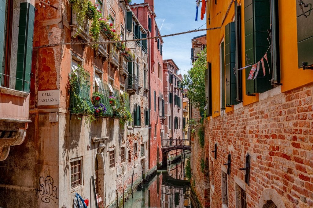 Kleiner Kanal in Venedig an einem sonnigen Tag, gesäumt von Fenstern mit Blumenkästen
