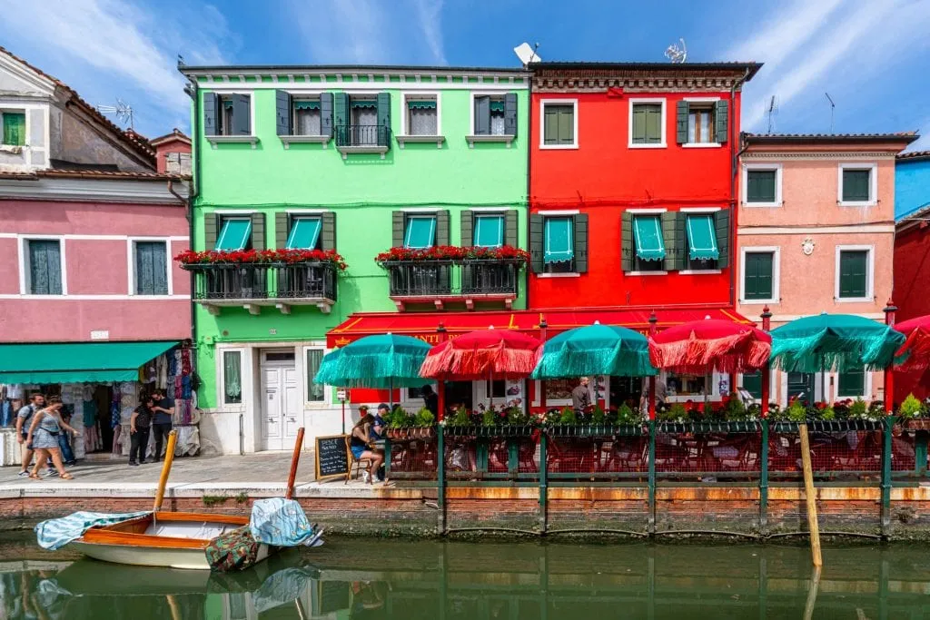 Photo of colorful houses in Venice with umbrellas and a canal out front.