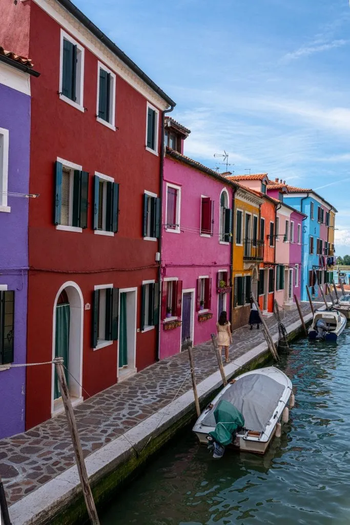 kate storm standing along a row of colorful houses in burano venice with canal to the right