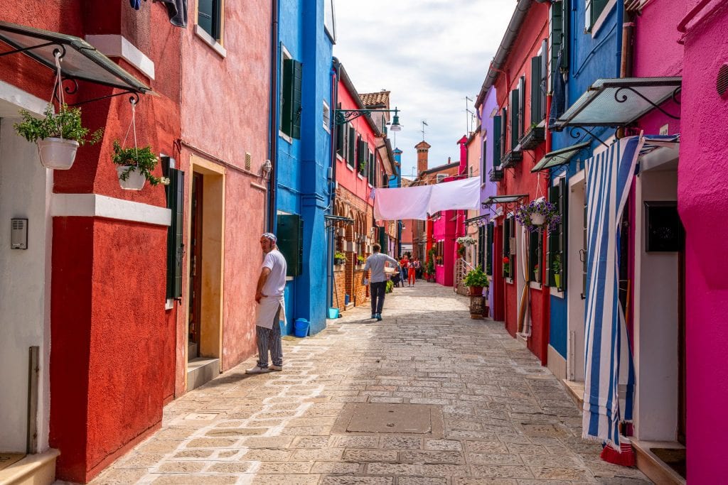 Photo of a colorful street in Burano with a man standing to the left, as seen on a trip to Burano from Venice.