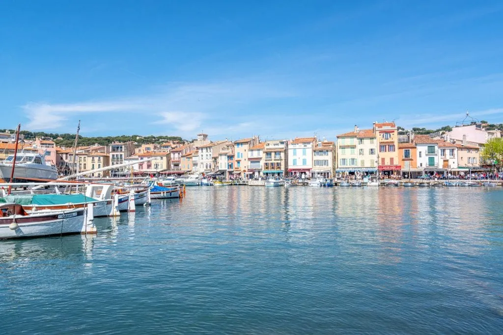 Port of Cassis with fishing boats on the left and buildings in the distance beyond the water.