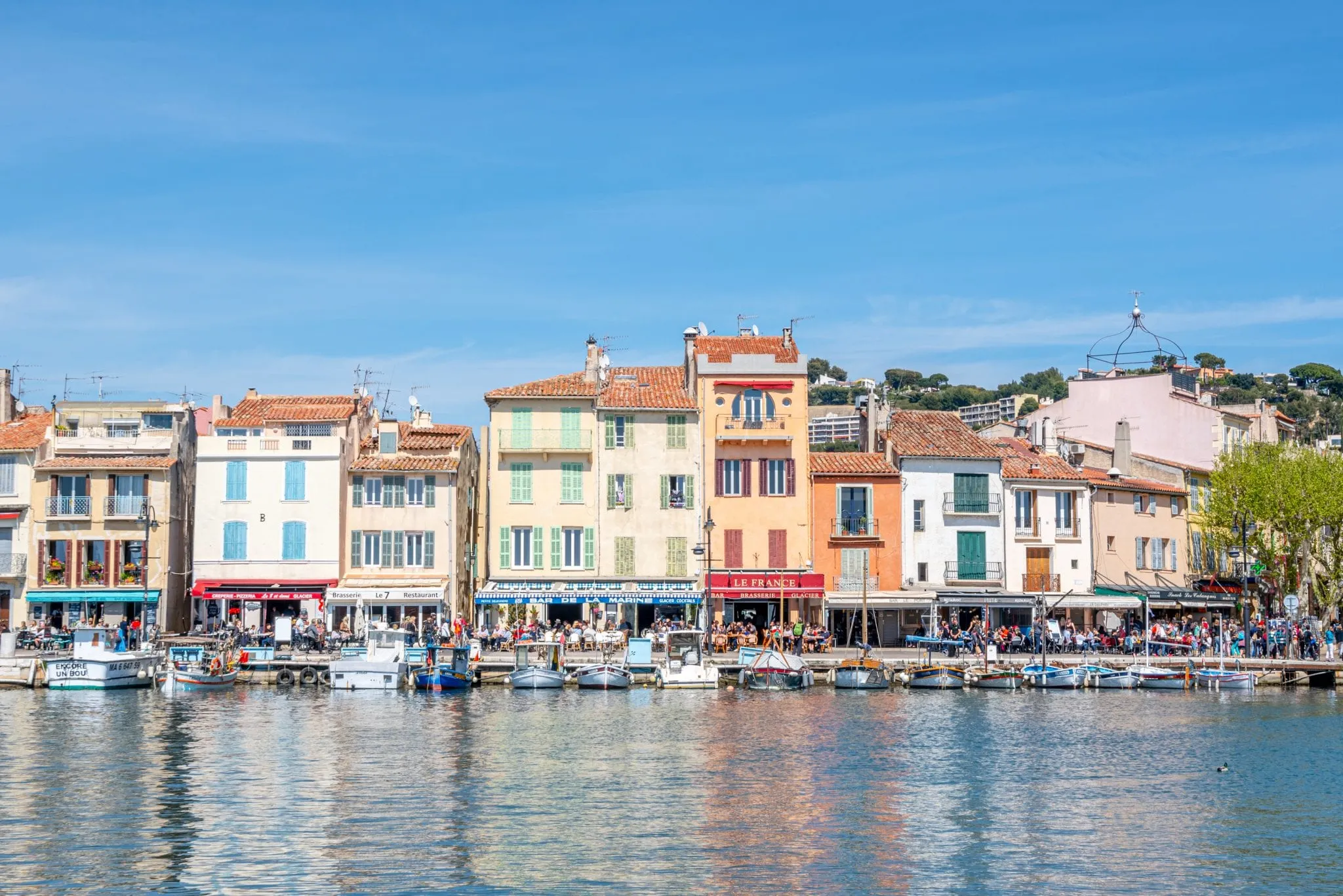 Buildings in front of harbor of Cassis France, their reflections are on the water in the bottom half of the photo.
