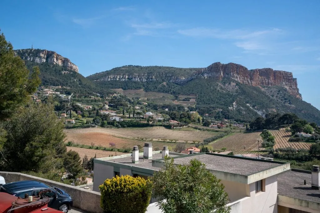 Countryside near Cassis France, with rooftops in the foreground and vineyards and cliffs in the background.