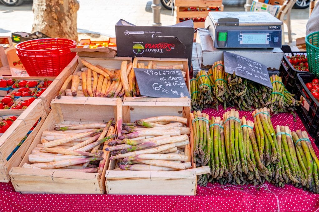 Boxes of white and green asparagus in front of a cash register at the outdoor food market in Aix-en-Provence