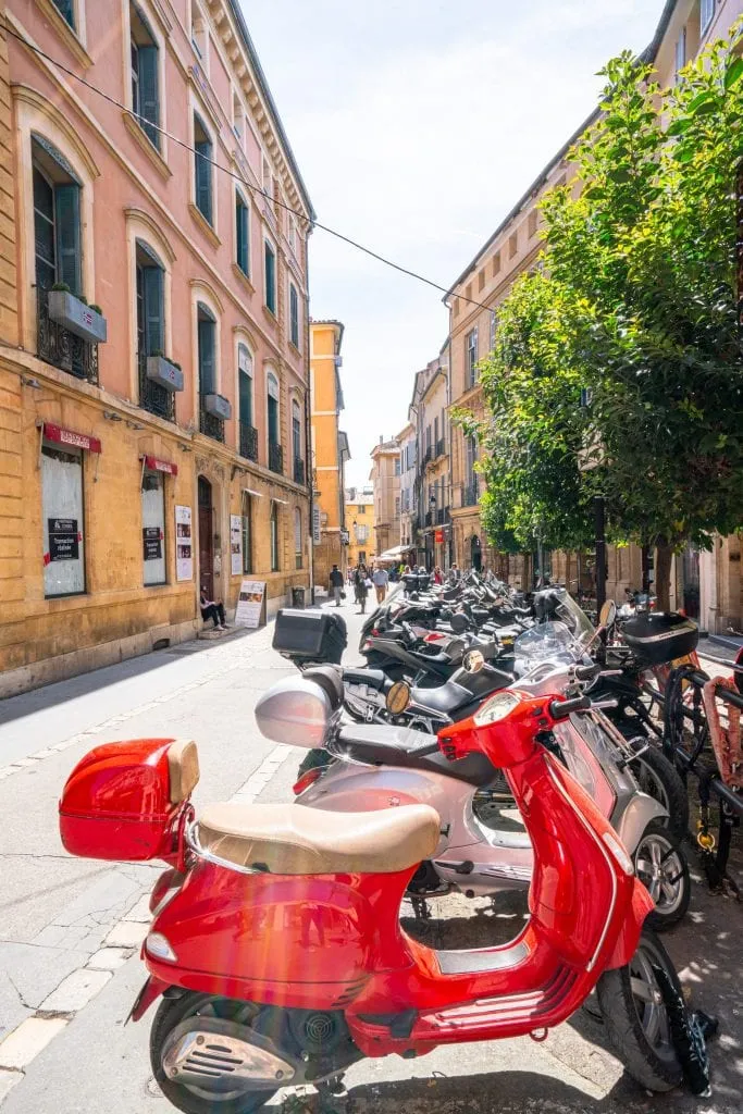 Street in Aix-en-Provence with a red Vespa in the foreground and a yellow building in the background