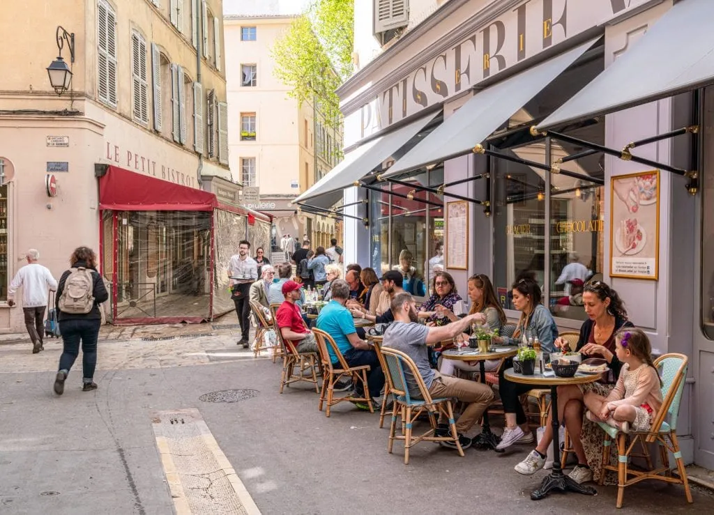 Street in Aix-en-Provence France, with a cafe to the right. The tables of the cafe are filled with visitors.