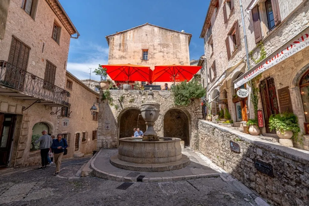 Photo of a square in Saint-Paul-de-Vence France--there's a red banner hanging over a restaurant in the center of the photo.