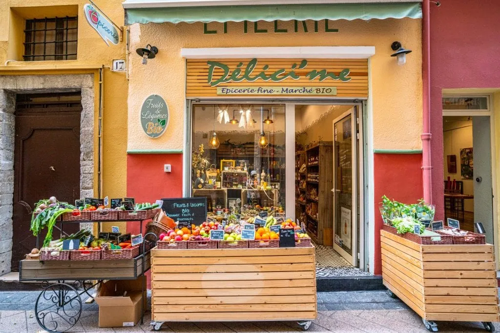 Deli in Nice France with a car full of fruits and vegetables parked in front of it.