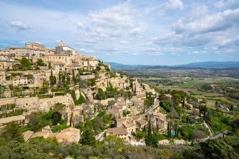 Photo of the village of Gordes France taken from above. The village is visible on the left and countryside on the right. Gordes is considered one of the best places to visit in the south of France!