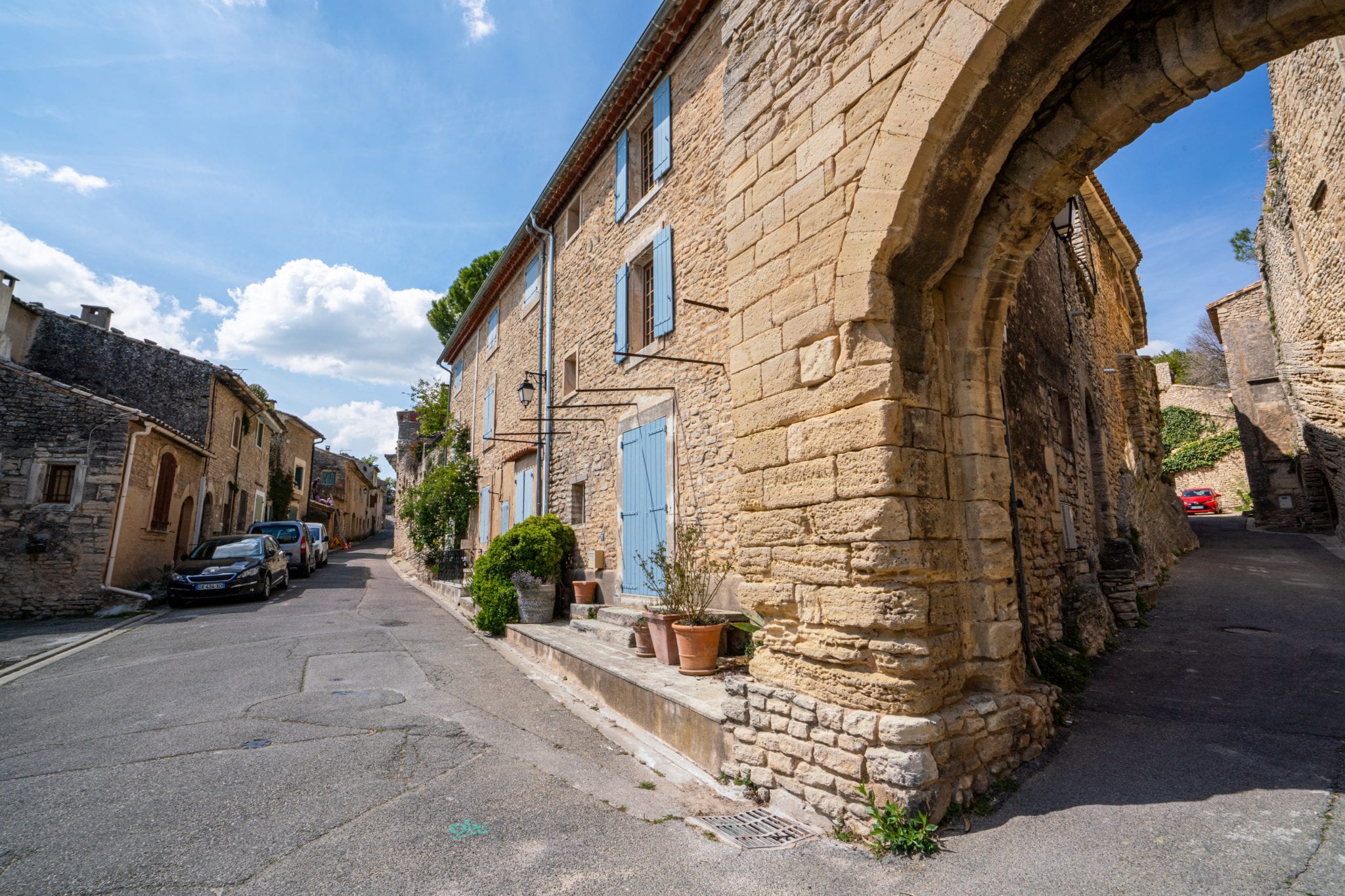 Street in Goult France with a stone building framed with blue shutters on the right