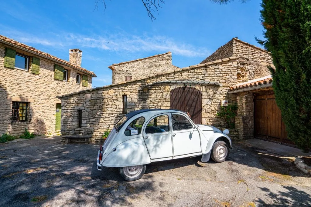 Photo of a small white car parked in Goult France. There are stone buildings visible behind the car.