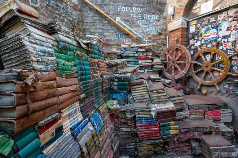 Staircase of books at Libreria Acqua Alta in Venice as seen from the side, two ship's wheels are propped up on the righthand side.