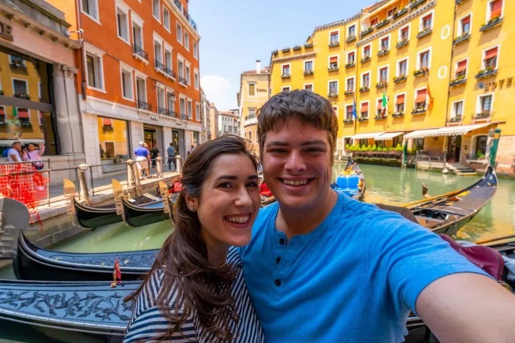 Couple taking a selfie in front of gondolas in Venice.