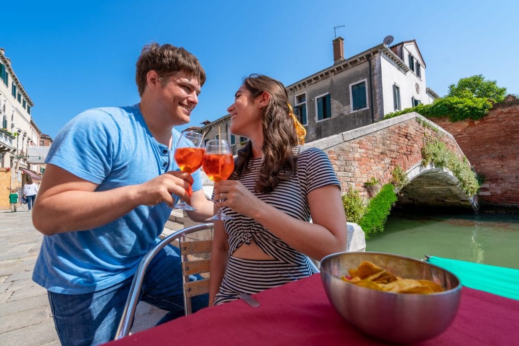 Paar stößt mit Aperol Sprtize in der Nähe einer Brücke in Cannaregio an