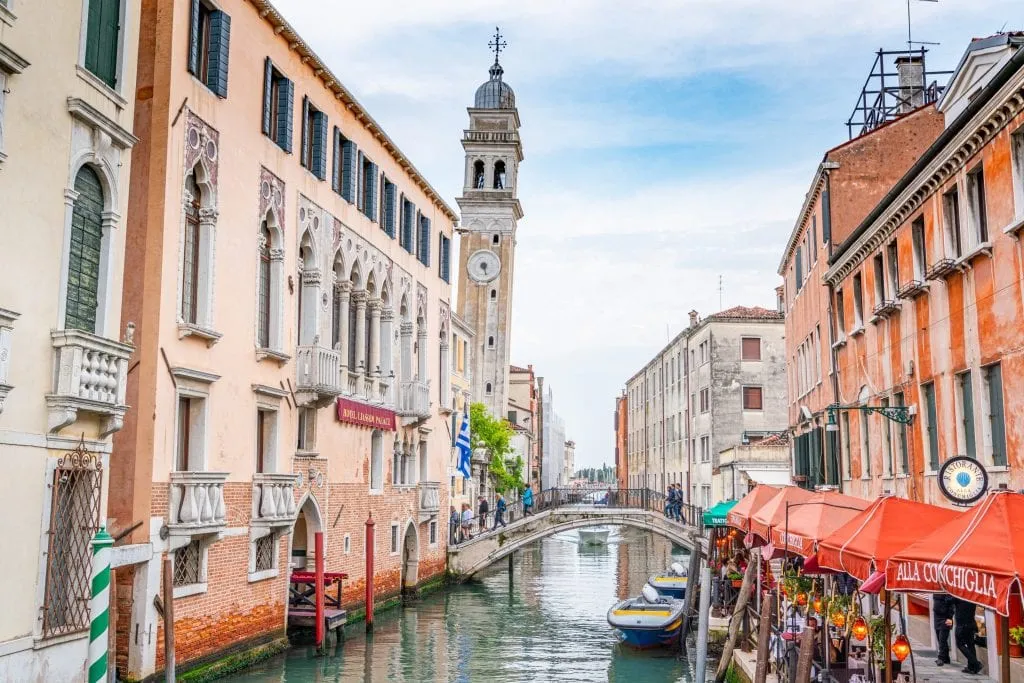Photo of Venice canal with leaning bell tower on the left side--seeking out Venice's leaning bell towers is a fun way to find hidden gems in Venice!
