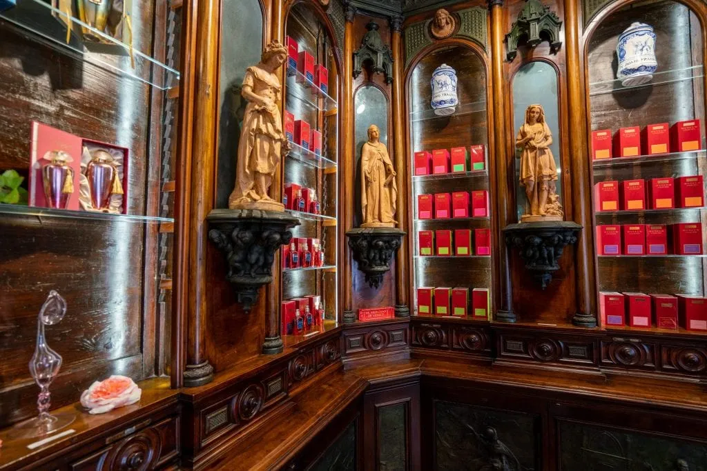 Interior of Merchant of Venice flagship store. There are red bottles of perfume lining the walls, and small stone statues of women decorating the shop.