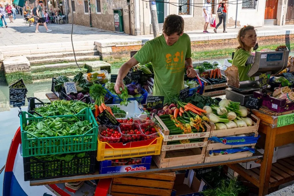 man in a green shirt selling vegetables at the venice dorsoduro vegetable barge