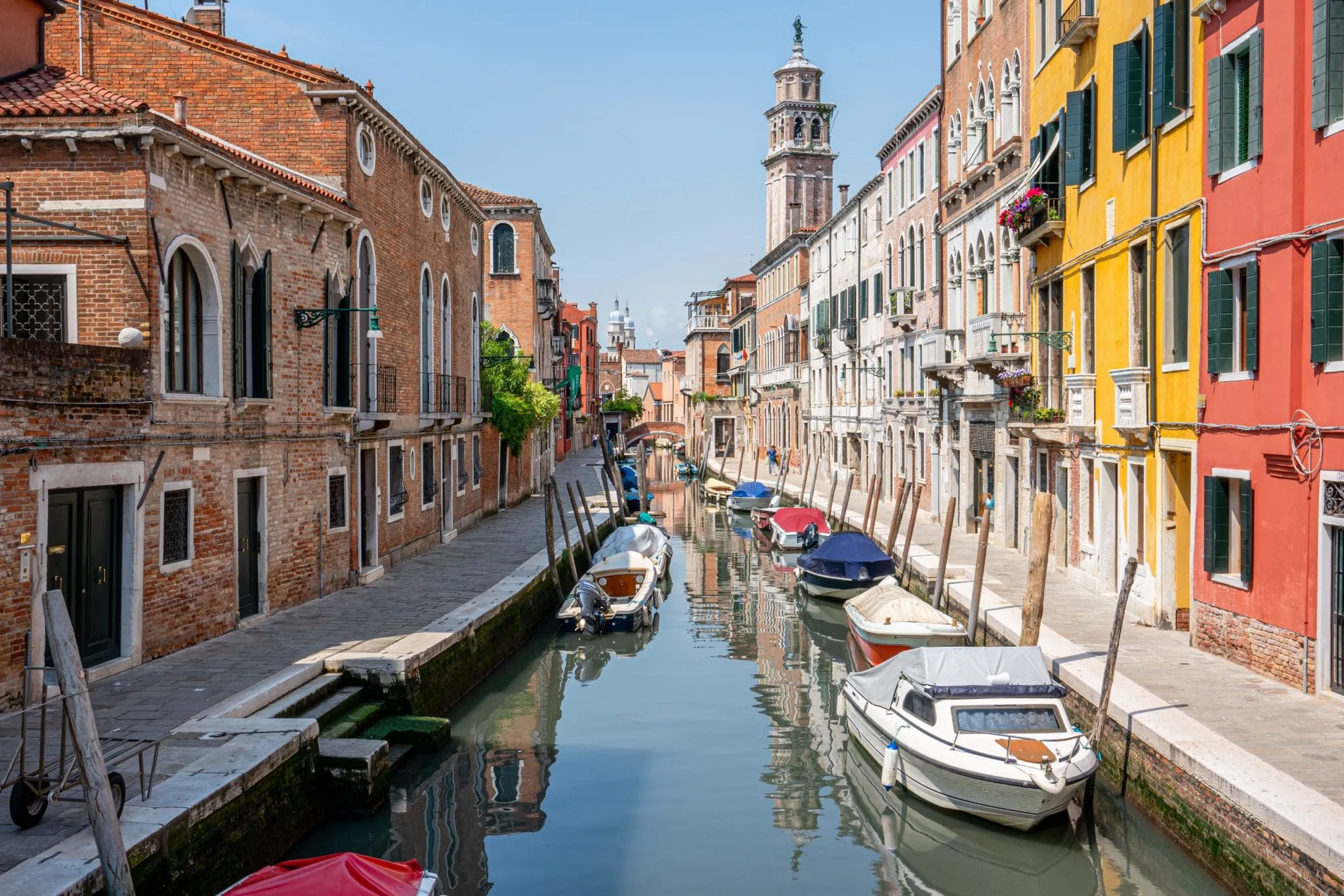 View of small canal in Dorsoduro Venice with colorful buildings to the right and motorboats parked in the canal. Quiet spots like this are common when seeking out Venice hidden gems