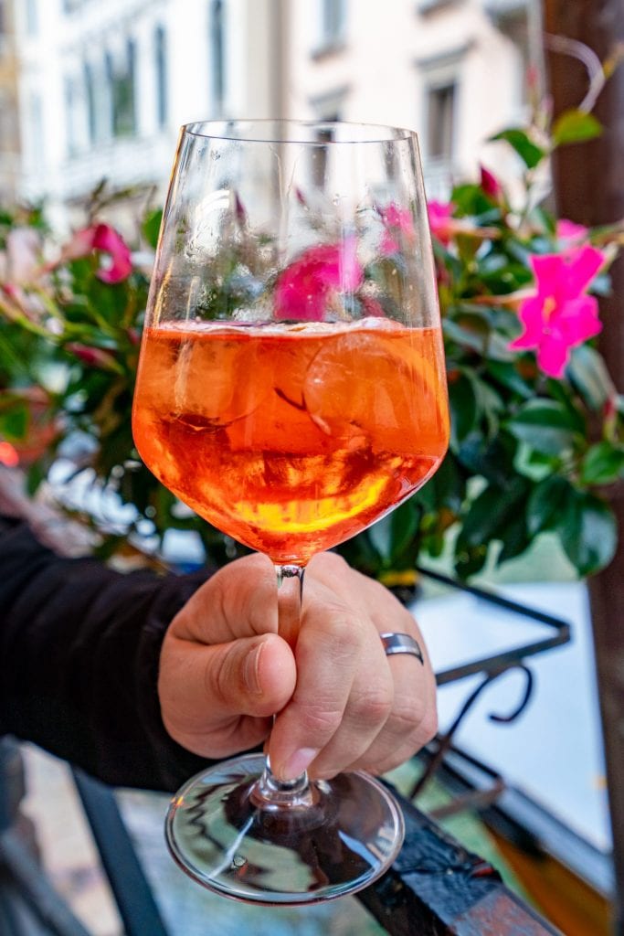 Nahaufnahme eines Aperol Spritz in Venedig, der vor rosafarbenen Blumen gehalten wird