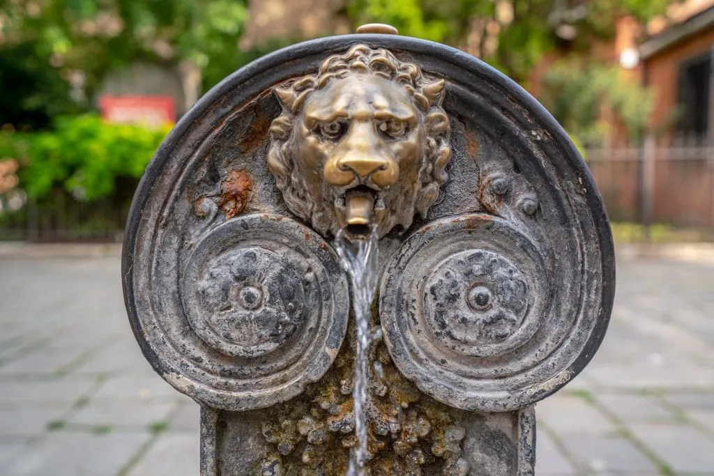 Photo of a small, pretty fountain with a lionhead spout as seen in Venice. One of many travel tips for Italy: you can drink from these fountains!