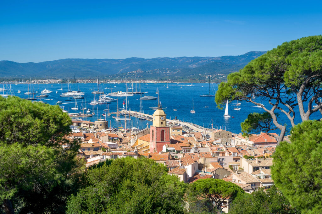 view of saint-tropez from above with village toward the foreground framed by trees and marina in the background, one of the most beautiful places in south of france to visit