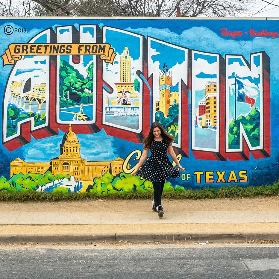 kate storm posing in front of the greetings from austin mural in austin texas