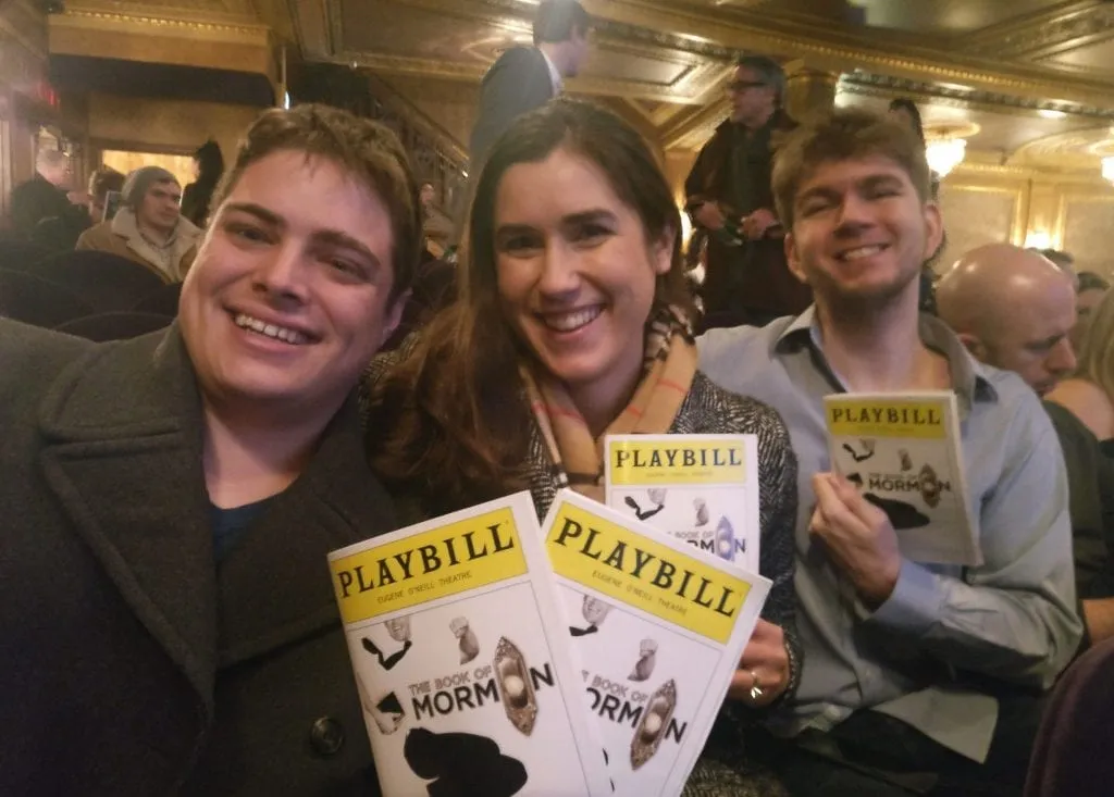 Kate and Jeremy with their friend Michael at a Broadway show, holding up playbills for the Book of Mormon