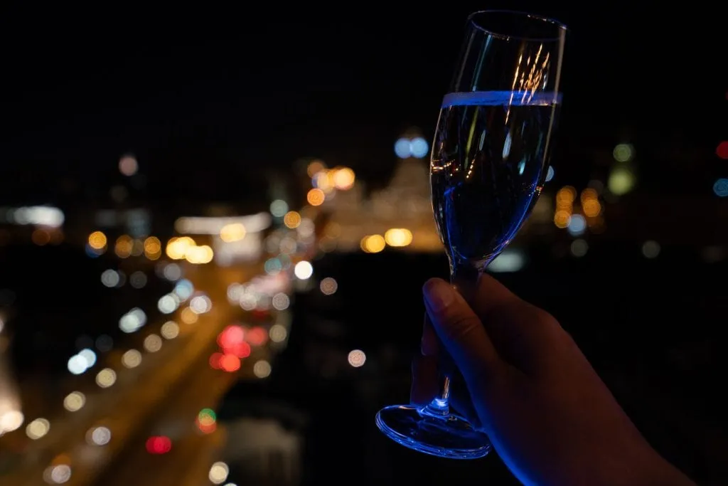 Glass of prosecco being held up over a busy Madrid street at night