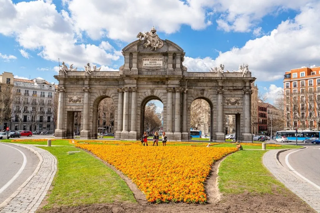 Puerta de Alcalá in Madrid Spain with yellow flowers in the foreground