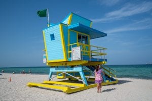 Kate in a pink dress standing in front of a blue art deco lifeguard stand on South Beach in Miami Beach.