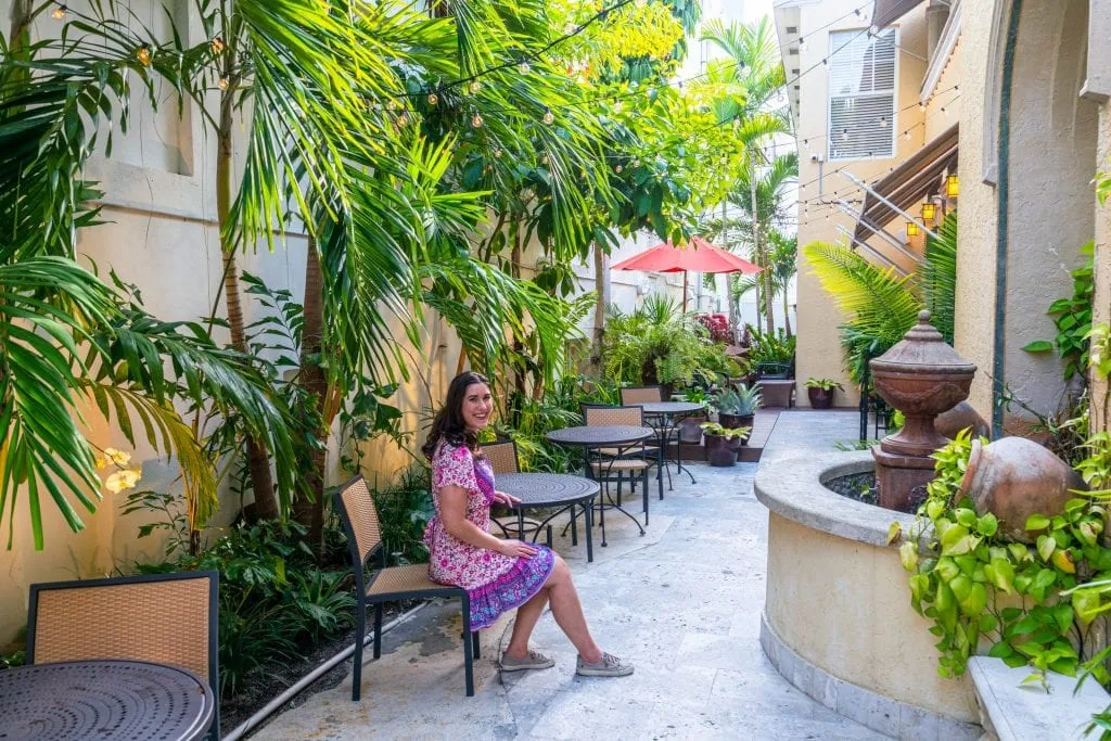 Kate in a pink dress sitting at a small table in front of Hotel Impala. The hotel is to the right.