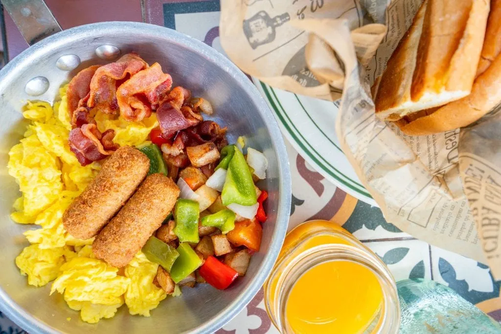 Big Havana Breakfast as served at Havana 1957 in Miami Beach, shot from above. A pan of eggs and croquetas, a basket of bread, a glass of orange juice.