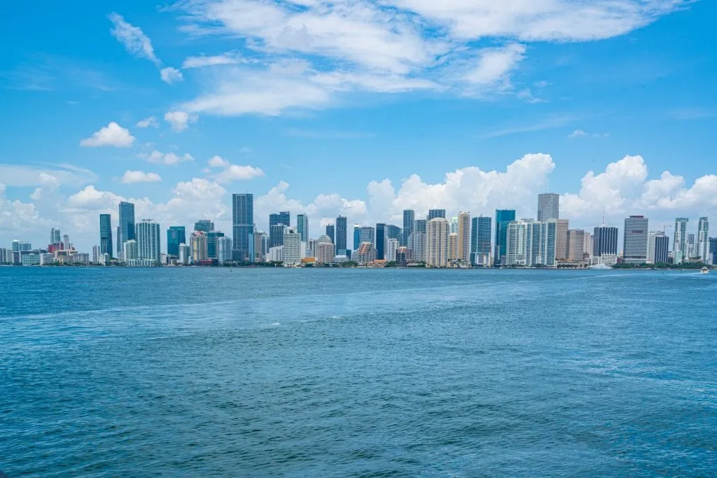 Skyline of downtown Miami as seen from across the Bay. The skyline is in the center of the photo, with water below and blue sky above.