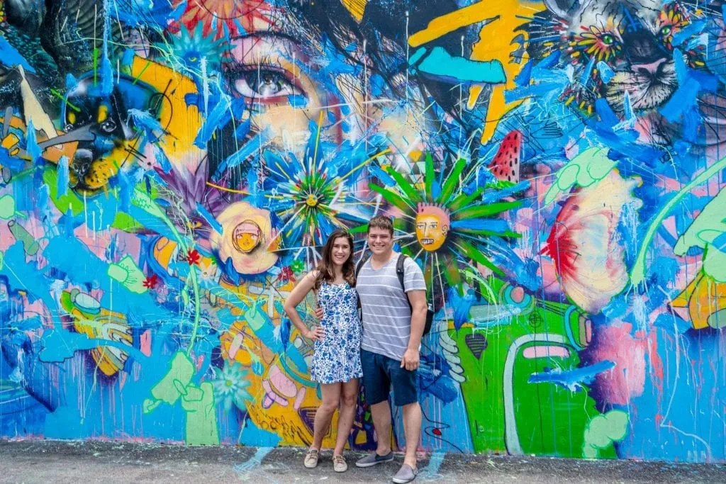 Kate and Jeremy standing in front of a colorful, mostly blue, mural in Wynwood, Miami