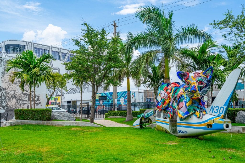 Colorful, painted plane on the ground in Wynwood Walls park. There is grass under the plane and palm trees behind it.