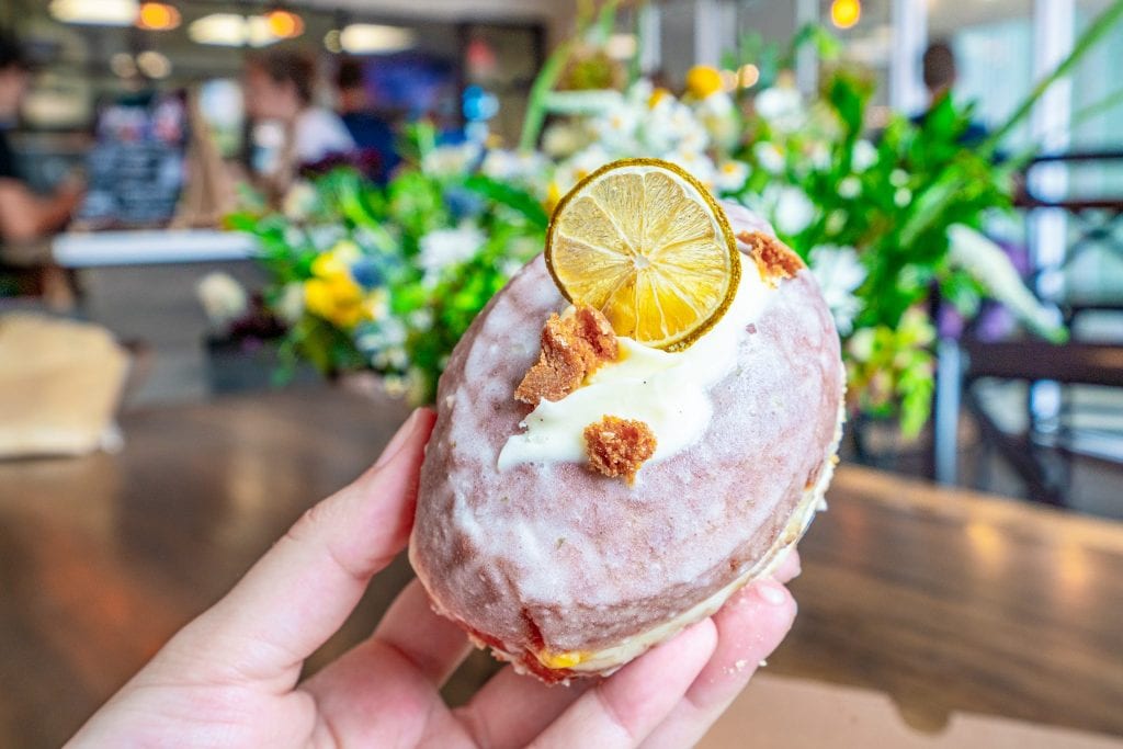 Key Lime pie donut as served at The Salty Donut in Wynwood, being held in front of a wooden table with a bouquet of flowers on it.