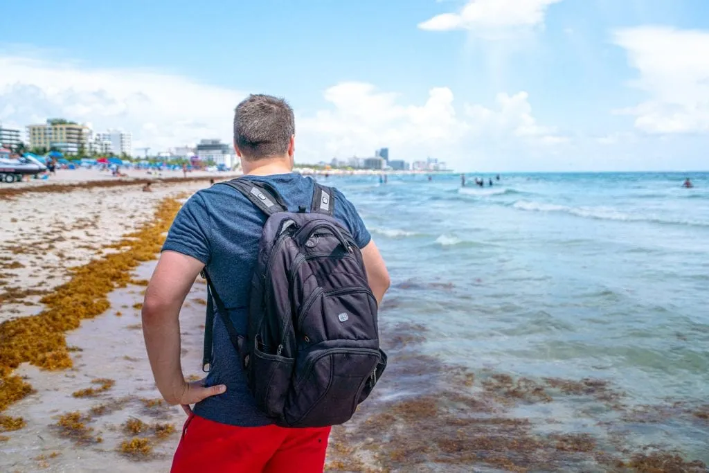 Jeremy standing with his back to the camera on South Beach. He's wearing a black backpack.