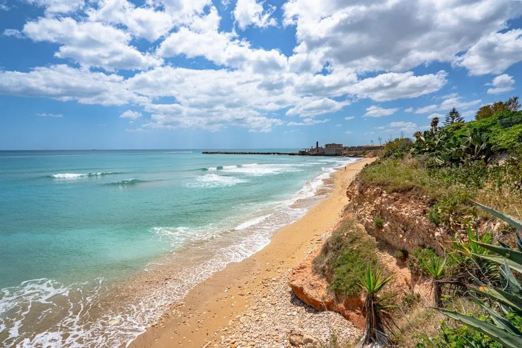 Long stretch of empty beach in Avola Sicily with the clear sea visible on the left, an excellent stop on any Sicily road trip itinerary