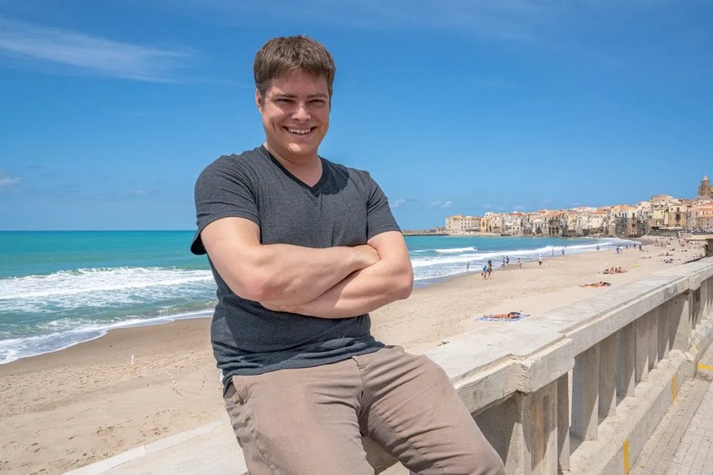 Jeremy Storm sitting on a wall overlooking Cefalu beach, a fabulous stop during a Sicily road trip itinerary