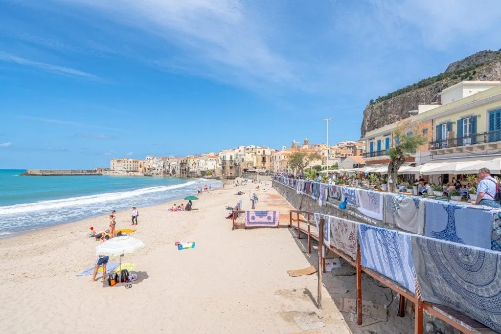 Cefalu Beach in Sicily Italy, with towels for sale on the right and the sea visible on the left, one of the best places to visit in Sicily travel