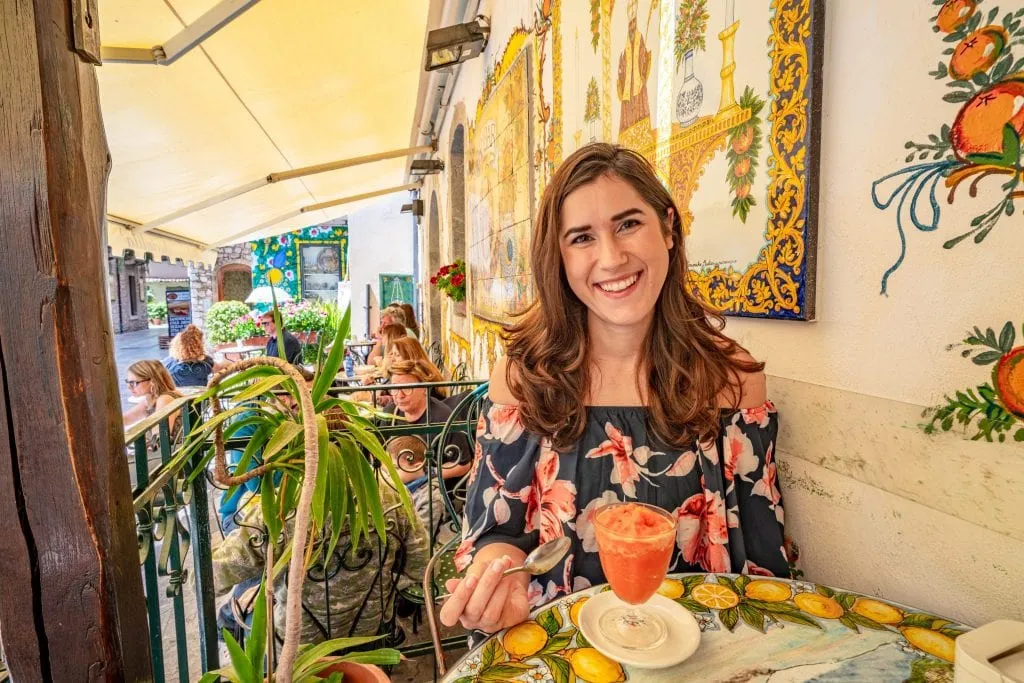 Kate Storm sitting a table at BamBar in Taormina. There's an orange granita in front of her and yellow tile work behind her. Visiting BamBar is absolutely one of the best things to do in Taormina Sicily!