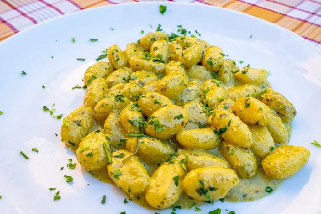 Photo of a plate of gnocchi served in Taormina Sicily. The gnocchi is on a white plate and has green garnish sprinkled on it.