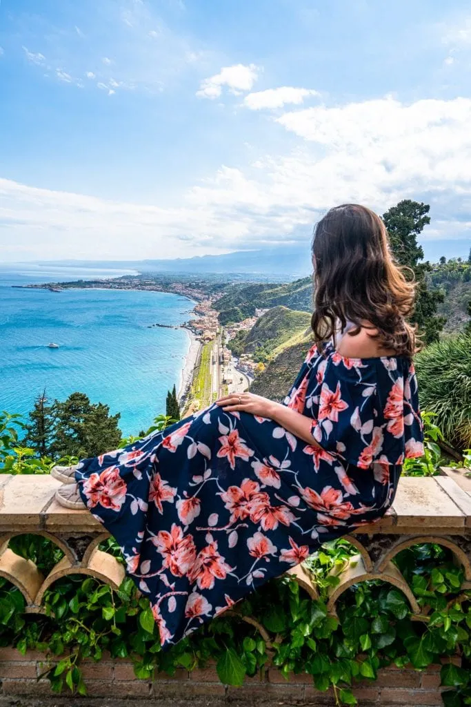 kate storm sitting on a garden wall in taormina sicily overlooking the ionian sea, one of the best places to visit in italy summer