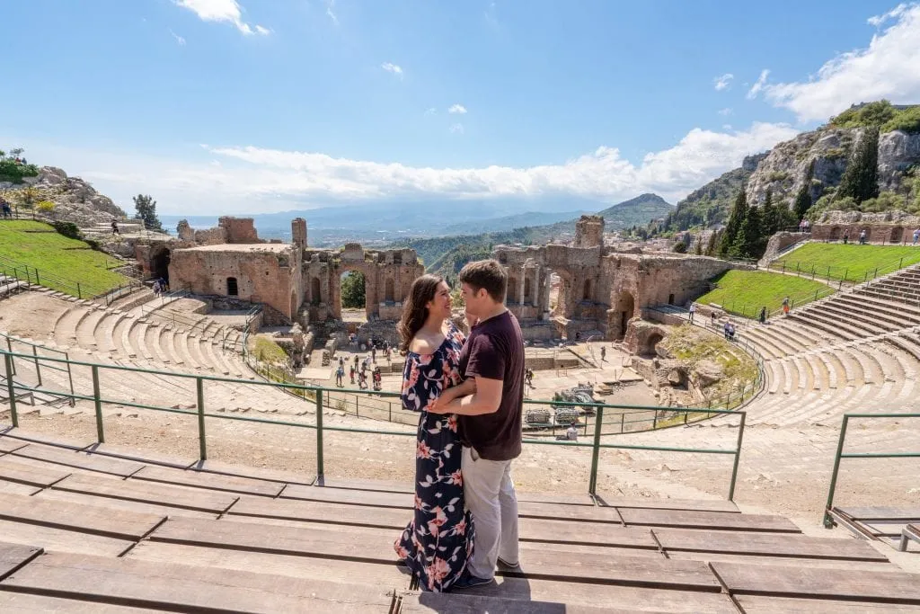 Kate and Jeremy standing in Greek Theatre in Taormina--visiting this place is easily one of the best things to do in Taormina! Kate and Jeremy are facing each other, Kate is wearing a floral maxi dress.