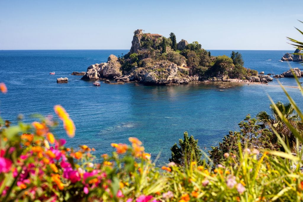 view of isola bella in taormina italy with colorful flowers in the foreground