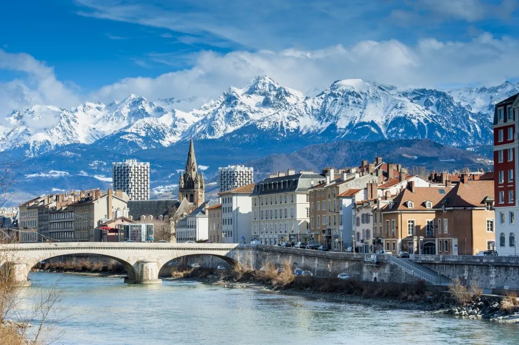 city of grenoble france with river in the foreground and snowcapped mountains in the background