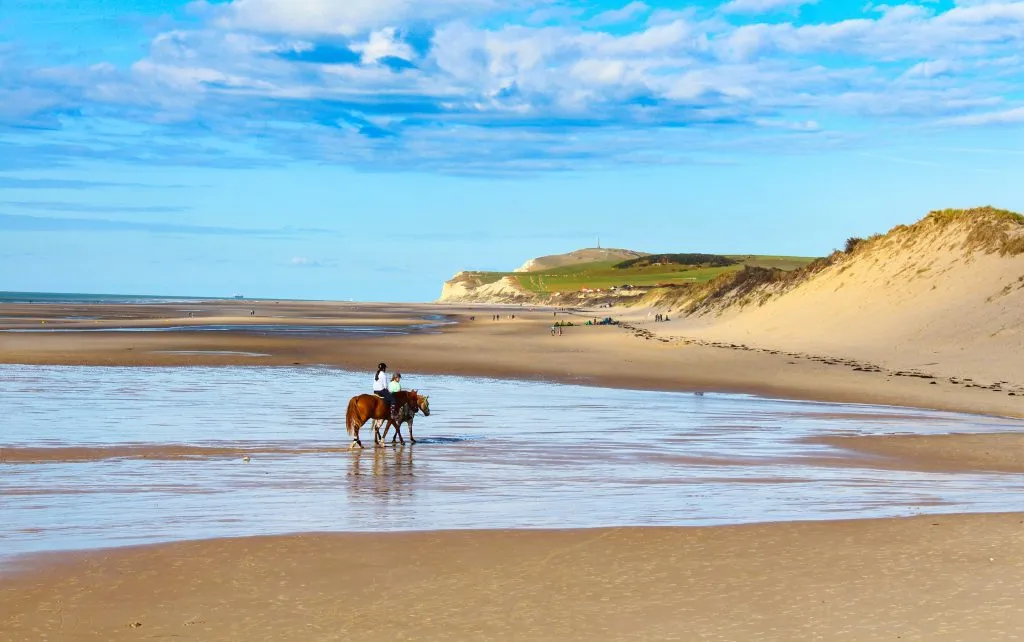 two people riding horses on a sandy stretch of the opal coast in northern france road trip